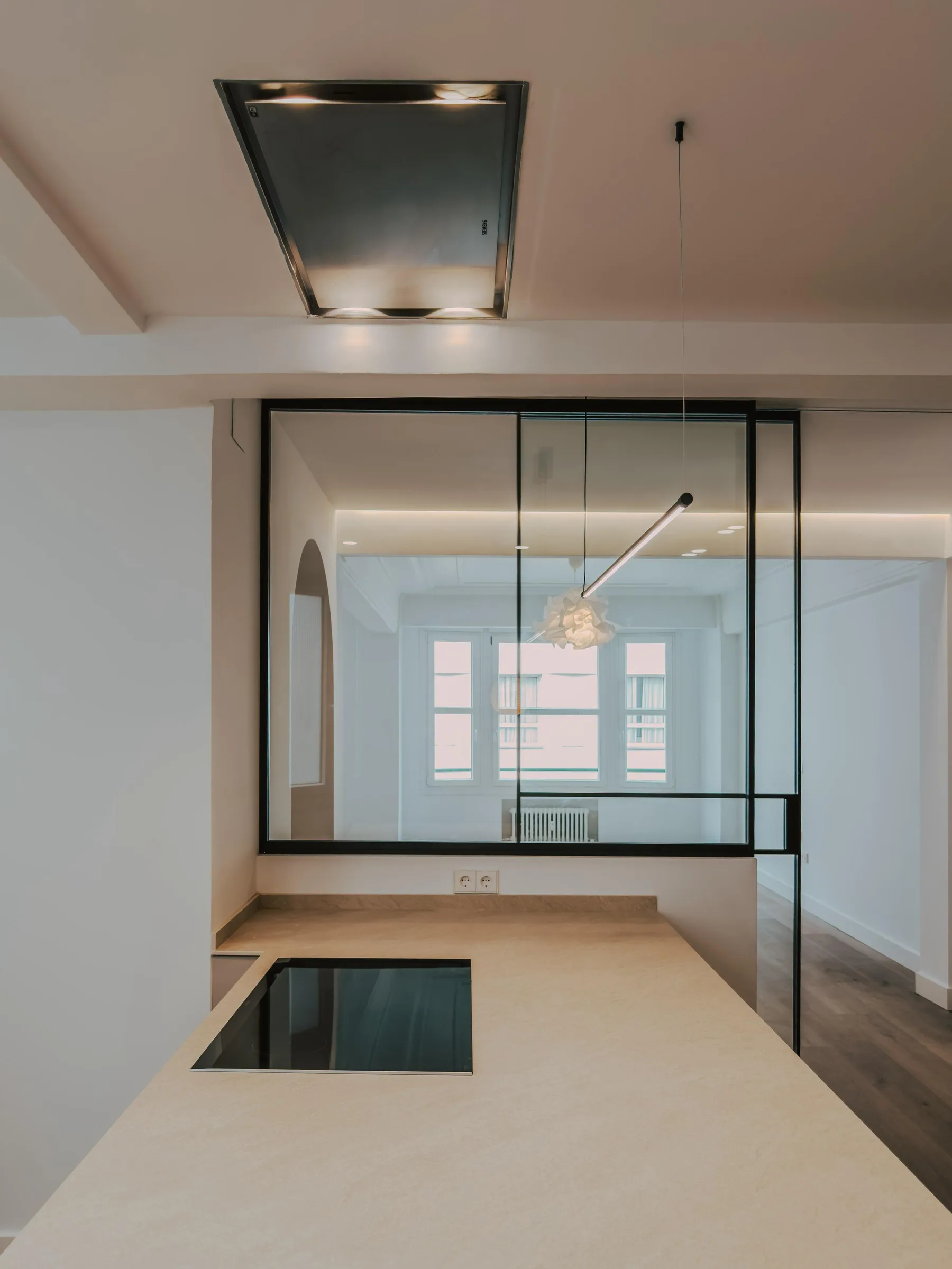 Cocina blanca con cerramiento de cristal y encimera clara de Suiteak